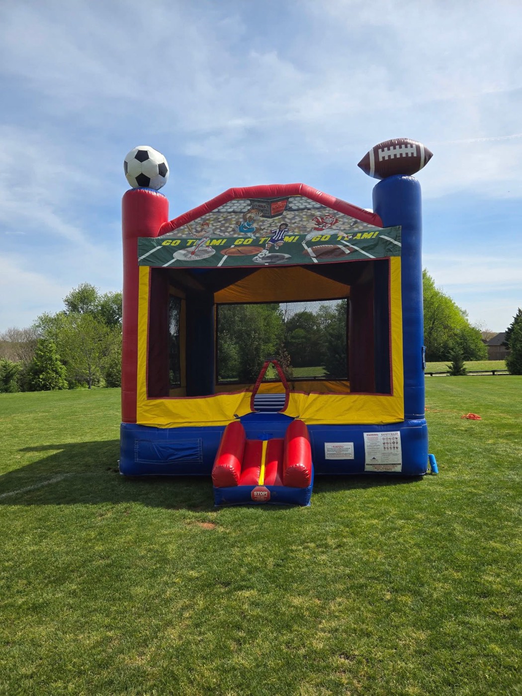 Red blue and yellow sports themed bounce house with soccer ball and football toppers